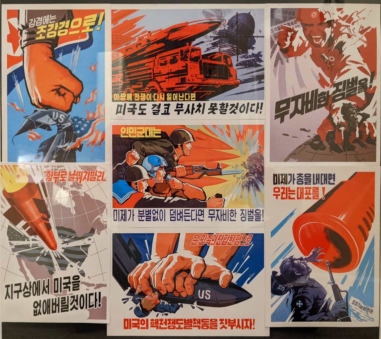 A collection of postcards I purchased and framed.
(Top-left): "Answer hardline pressure with an even harder line!"
(Bottom-left): "If they recklessly run wild, we will wipe America from the face of the earth!"
(Top-center): "If war breaks out again on this land, America will certainly not escape unharmed!"
(Center): "The People's Army: if the U.S. imperialists recklessly attack, merciless punishment!"
(Bottom-center): "With the united strength of the whole nation, let us crush the U.S. imperialists' schemes to provoke nuclear war!"
(Top-right): "Merciless punishment!"
(Bottom-right): "If the U.S. imperialists point guns at us, we answer with cannons!"