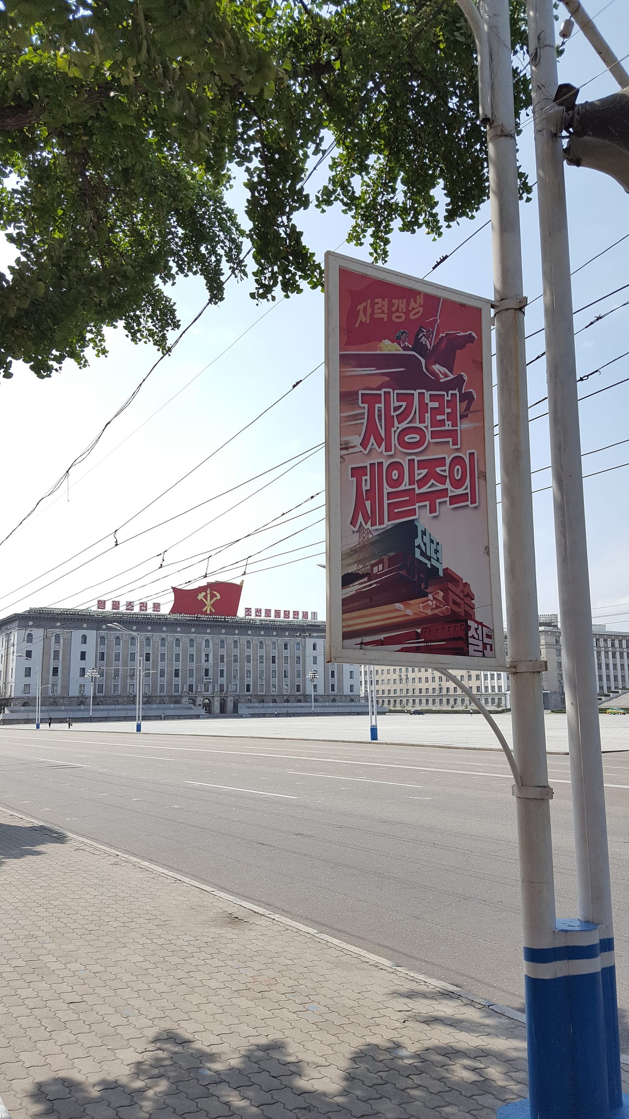 Walking around Kim Il Sung Square. Reads: "Self-Reliance First!"