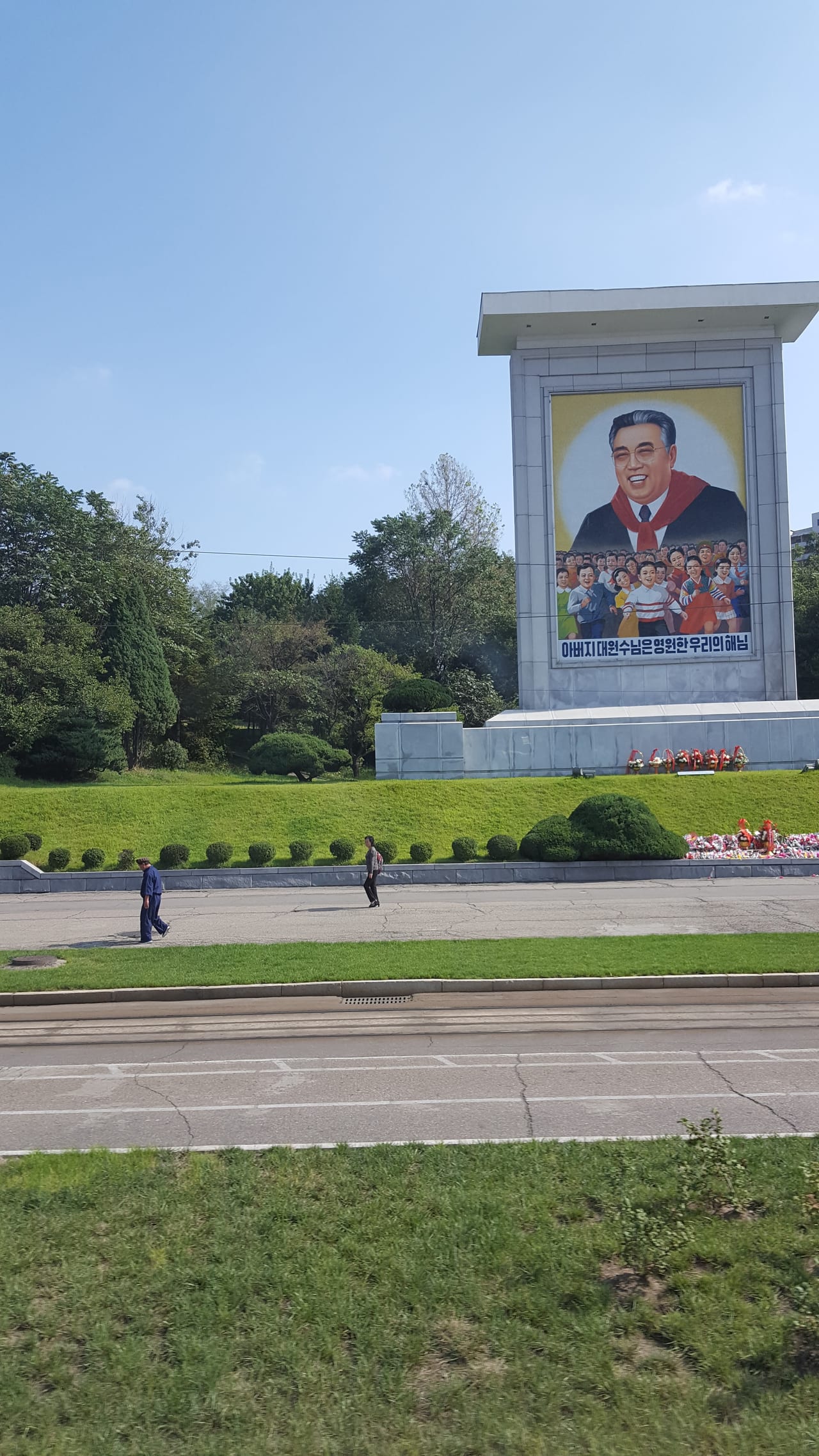 Streetside propaganda seen on the way to the theater. "Father Generalissimo is our eternal Sun". "Father Generalissimo" refers to North Korea's founder, Kim Il-sung. He is depicted wearing the red neckerchief of the Korean Children's Union, a common motif portraying him as a father figure to the nation's youth.