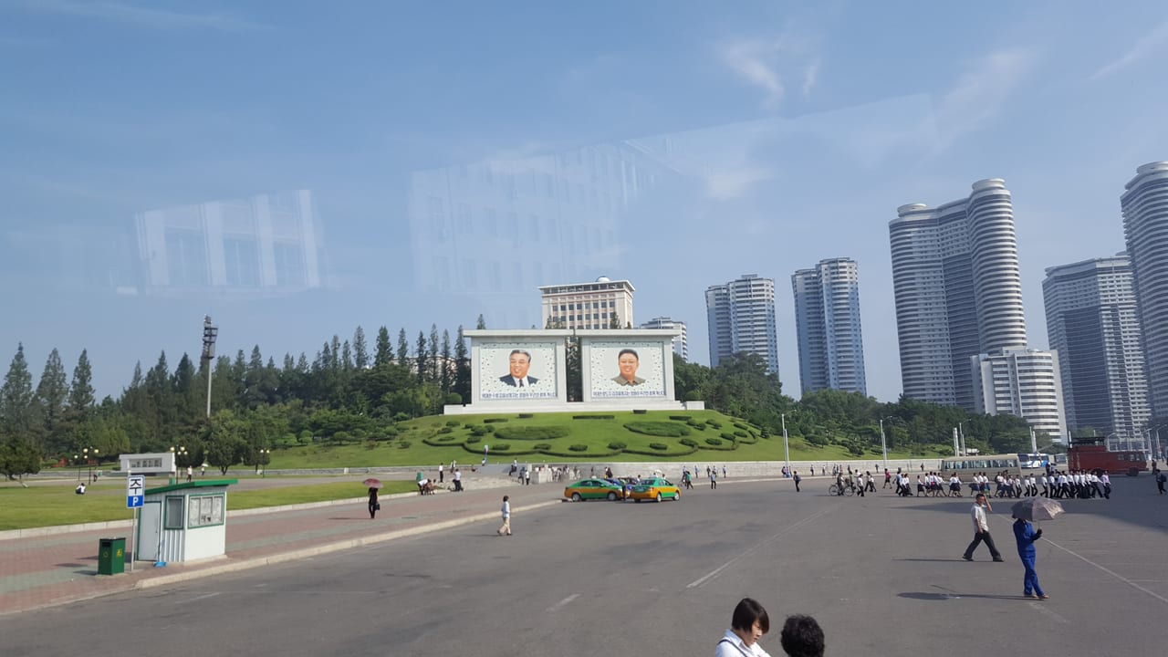 Street-side portraits of Kim Il Sung and Kim Jong Un just north of the Grand People's Study House viewed from our bus on the way to the Mansudae Hill Grand Monument.