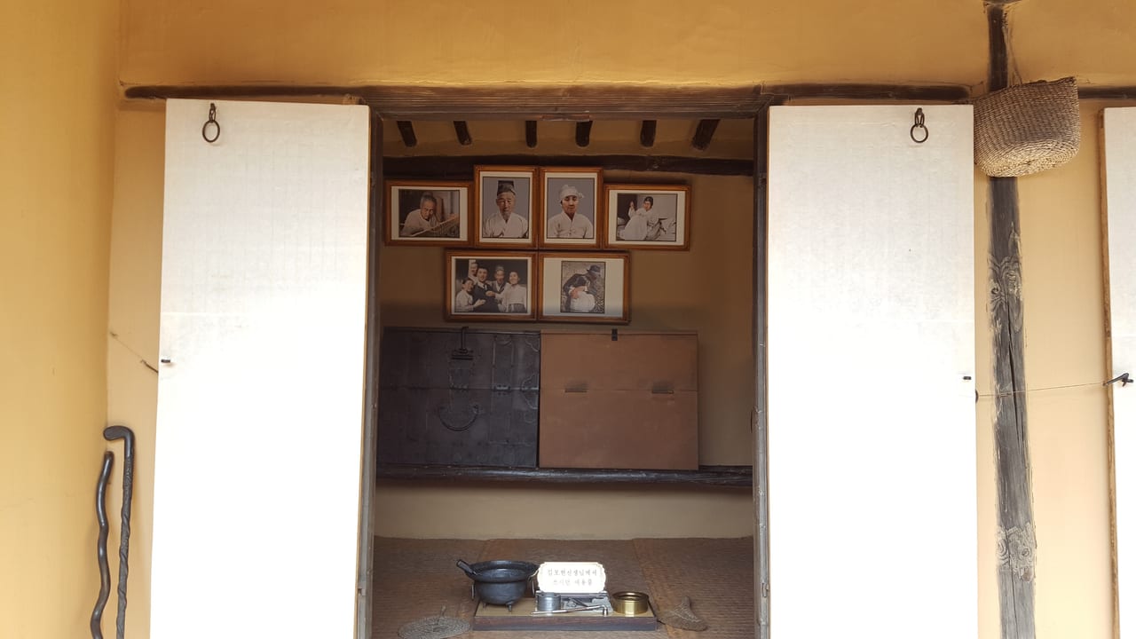 The "Main Room" containing six family portraits over storage chests with household items. The placard reads that it contains household items used by Kim Bo-hyon, Kim Il Sung's grandfather.