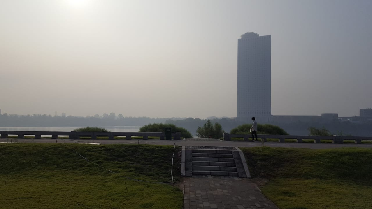 Woman walking with Yanggakdo International Hotel set in the smoggy background.